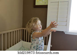 Pouting preschooler girl reaching out of crib