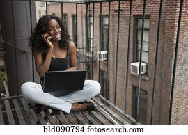 Black woman using laptop and cell phone on fire escape