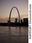 Arch landmark next to urban river at sunset