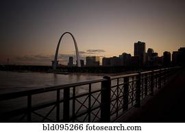 Arch landmark next to urban river at sunset
