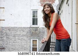 Mixed race woman leaning on fire escape railing