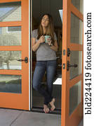 Woman standing barefoot in doorway drinking coffee
