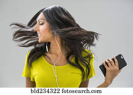 Carefree Indian woman tossing hair and listening to music