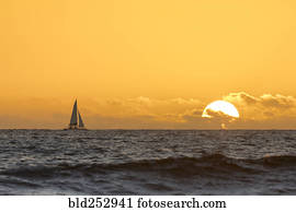 Distant sailboat in ocean at sunset