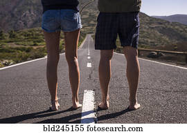 Legs of barefoot Caucasian couple standing in middle of road