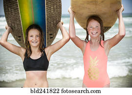 Portrait of smiling girls balancing surfboards on top of heads