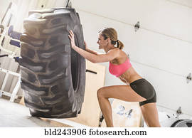Woman pushing heavy tire in gymnasium