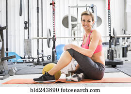 Woman sitting with heavy ball on exercise mat in gymnasium