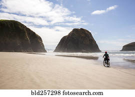 Distant Caucasian woman riding bicycle on beach