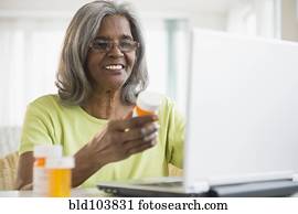 African American woman holding pill bottle and using laptop