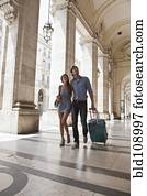 Caucasian couple pulling luggage in city