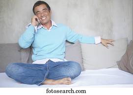 Mid adult man sitting on a bed talking on a mobile phone