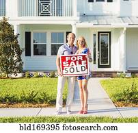 Caucasian couple holding sold sign outside new home
