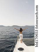 Woman standing with arms outstretched on sailboat deck