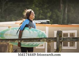 African American woman carrying surfboard outdoors