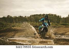 Caucasian man riding dirt bike in puddle