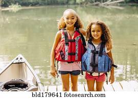 Mixed race sisters wearing life jackets at lake
