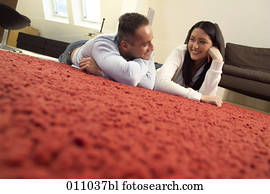 Young couple lying on the carpet of their living room looking at each other Young couple lying on the carpet of their living room looking at each other