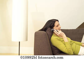 Young woman talking on mobile phone while lying on the sofa Young woman talking on mobile phone while lying on the sofa