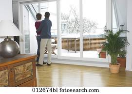 mature couple looking out of the window of their living room mature couple looking out of the window of their living room