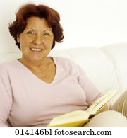 Mature woman sitting on sofa reading with dog beside her Stock Image