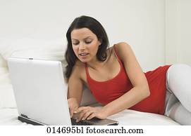 young woman lying on bed with laptop computer young woman lying on bed with laptop computer