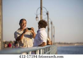 Man photographing woman on pier