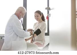 Doctor checking teenage patient’s blood pressure with cuff in examination room 