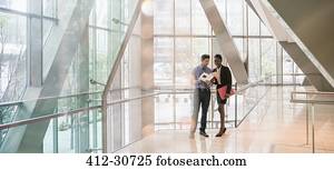 Corporate businessman and businesswoman discussing paperwork in modern lobby