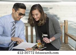 Corporate businessman and businesswoman eating lunch and reviewing paperwork on bench