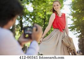 Man photographing woman in park