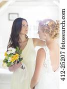 Bridesmaid helping bride with hairstyle in bedroom