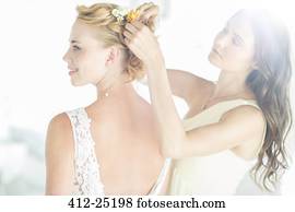 Bridesmaid helping bride with hairstyle in garden