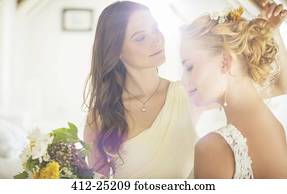 Bridesmaid helping bride with hairstyle in bedroom