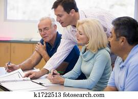 Adult students in class with teacher helping (selective focus) Adult students in class with teacher helping (selective focus)