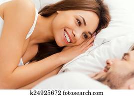 Good morning! Top view of beautiful young loving couple lying in bed and looking at each other with smile
