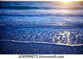 Sunset over a calm ocean with lapping waves