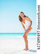 Full length portrait of smiling young woman applying sun screen creme