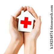 hands holding paper house with red cross hands holding paper house with red cross