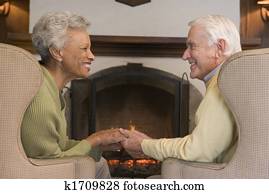 Couple sitting in living room by fireplace holding hands and smiling