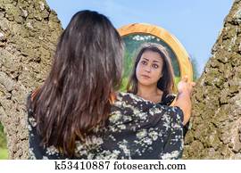 Woman looking in mirror between trees