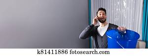 Man Collecting Water In Bucket While Calling Plumber Man Collecting Water In Bucket While Calling Plumber