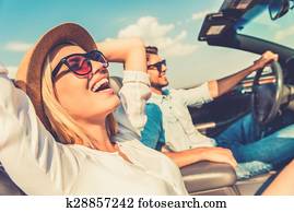 Freedom of the open road. Side view of joyful young woman relaxing on the front seat while her boyfriend sitting near and driving their convertible 