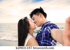 Couple taking self portrait photos with smart phone on the beach