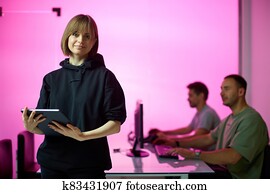 Young girl designer and his creative design team at the office during developing a new project, pink neon background Young girl designer and his creative design team at the office during developing a new project, pink neon background