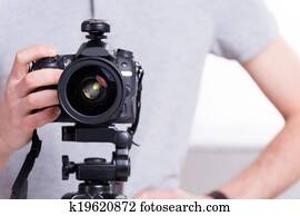 Ready to shoot. Close-up of man holding digital camera while standing in studio with lighting equipment on background 