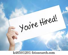 You're Hired! Sign on white paper. Man Hand Holding Paper with text. Isolated on sky background