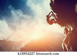 A silhouette of man climbing on rock, mountain at sunset. 