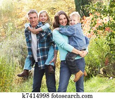 Family Group Outdoors In Autumn Landscape With Parents Giving Chiildren Piggyback Family Group Outdoors In Autumn Landscape With Parents Giving Chiildren Piggyback