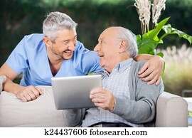 Laughing Caretaker And Senior Man Using Tablet Computer